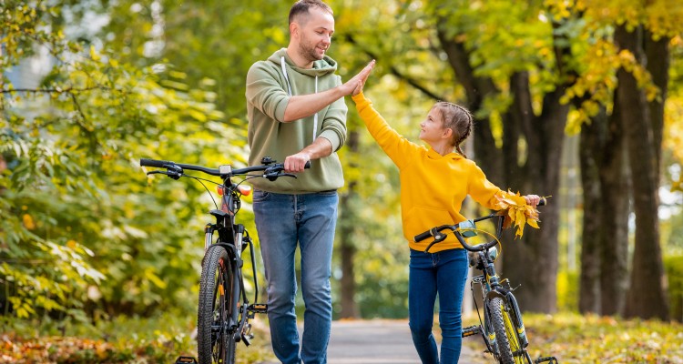 En man och en yngre flicka leder sina cyklar. De är glada och gör en high five.