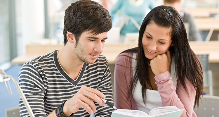 En manlig och en kvinnlig student i klassrum tittar ner i en bok och ler