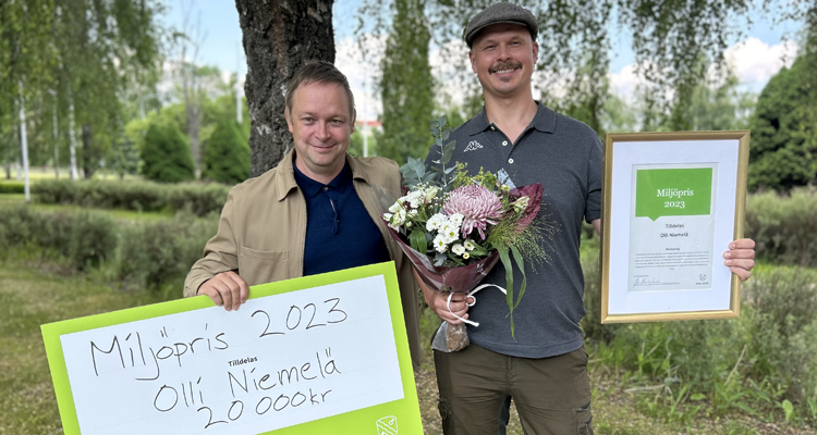 Två personer står bredvid varandra med blommor, ett diplom och en prischeck på 20 000 kronor.