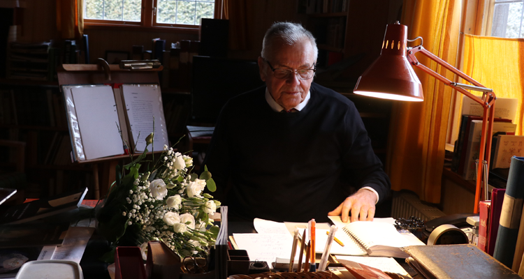 En äldre man sitter vid sitt stora skrivbord och tittar ner i några papper