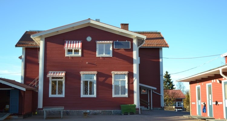 Faluröd byggnad, fem fönster och röd- och vita markiser ovanför fönstren 