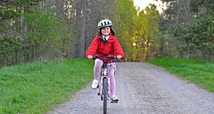 Flicka cyklar på skogsväg. Foto.