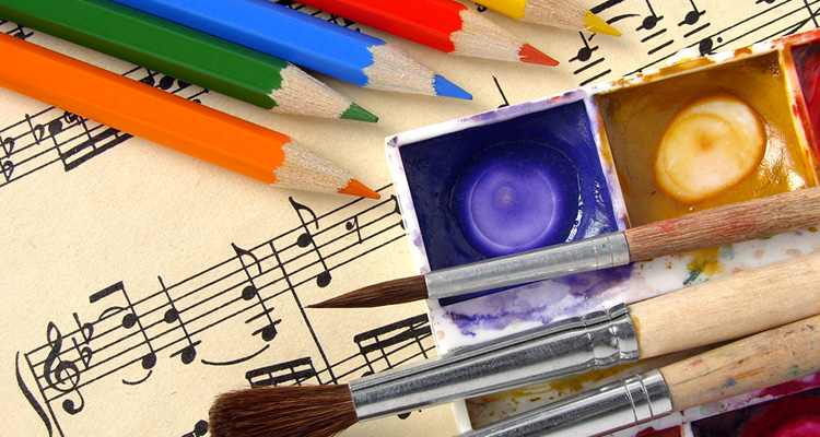 Färgpennor, akvarellfärger och penslar liggandes på ett papper med musiknoter.